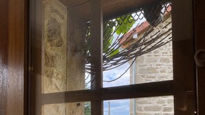 A wooden-framed window with a view of a stone building, outdoor furniture, and a garden.