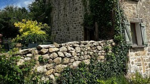 A stone building with ivy-covered walls, a stone wall in front, and a window with shutters.