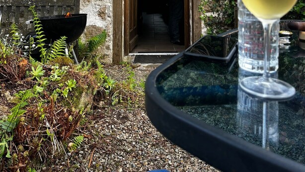 A stone building with a wooden door and a glass table with a wine glass.