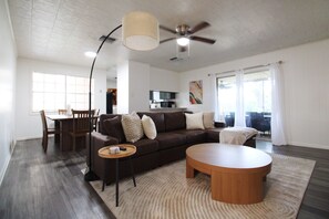 A modern living room with a brown leather sofa, a wooden coffee table, and a dining area with a wooden table and chairs. - 15% ALL OF JULY! Spacious Screened- In Porch Perfect for Group Stays (Houma)