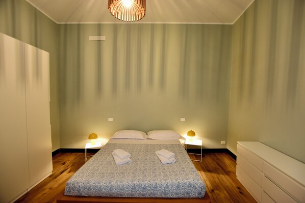 A bedroom with a bed, two bedside tables, and a hanging light fixture.