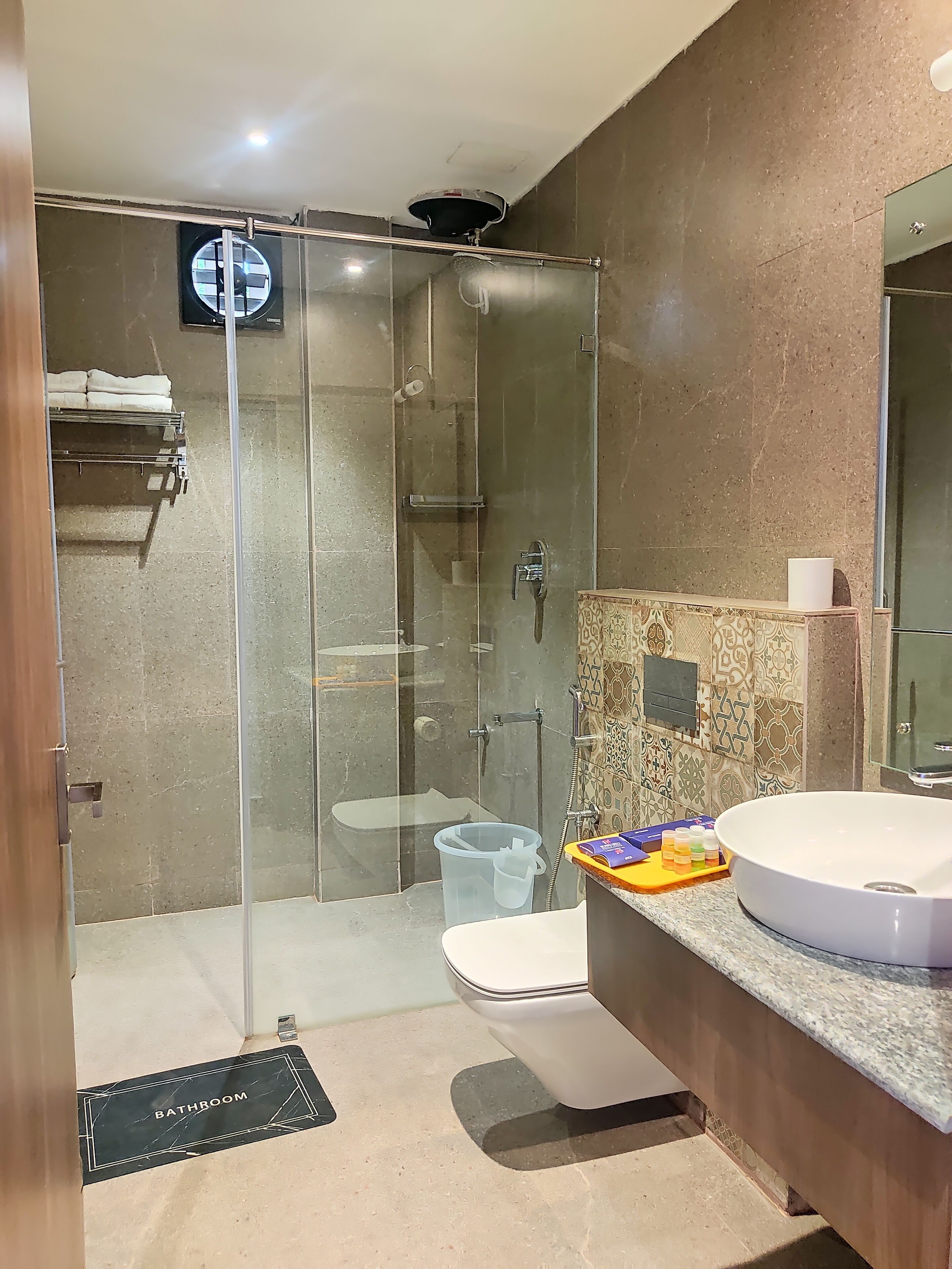 Un baño moderno con ducha envuelta en vidrio, un lavabo blanco y un mueble de tocador con un salpicadero estampado.