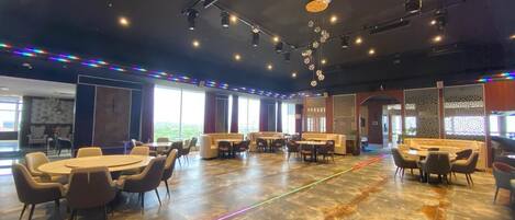 A spacious conference room with round tables and chairs, large windows, and a modern ceiling design.