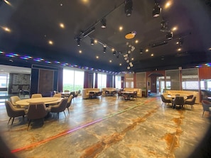 Een ruime vergaderzaal met ronde tafels en stoelen, grote ramen en een modern plafondontwerp.