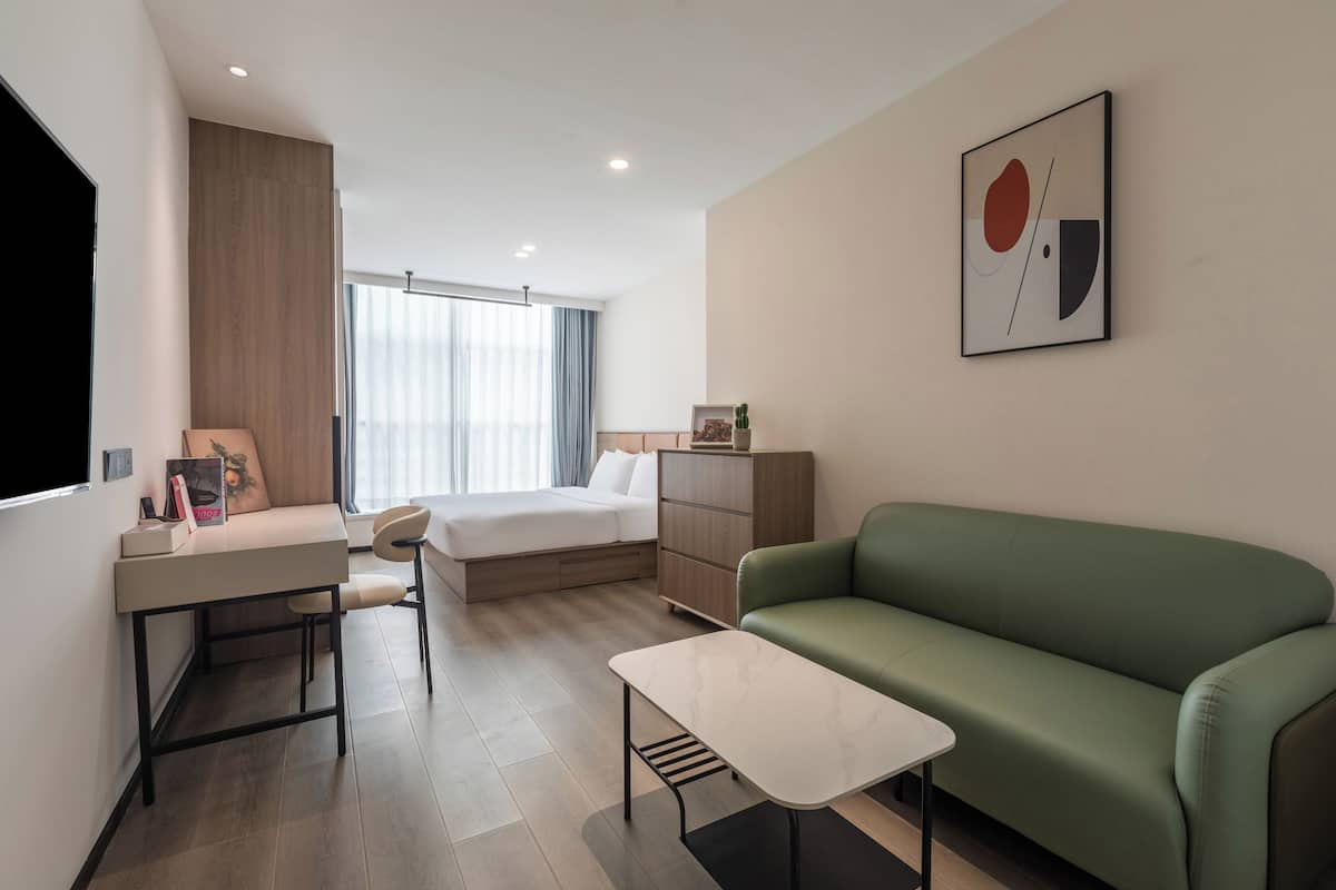 Una habitación de hotel moderna con una cama, un sofá verde, un escritorio pequeño y un televisor de pared.