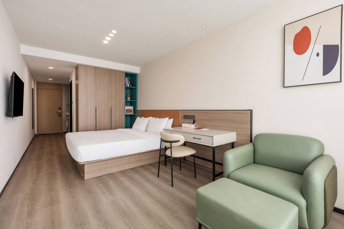 Una habitación de hotel moderna con cama, escritorio, silla y sofá verde.
