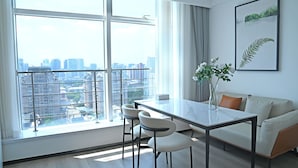 A modern living room with a large window, a dining table, two chairs, a sofa, and a framed plant on the wall. - Beijing Chengying Hotel - Sanlitun Taikoo Li (Beijing)