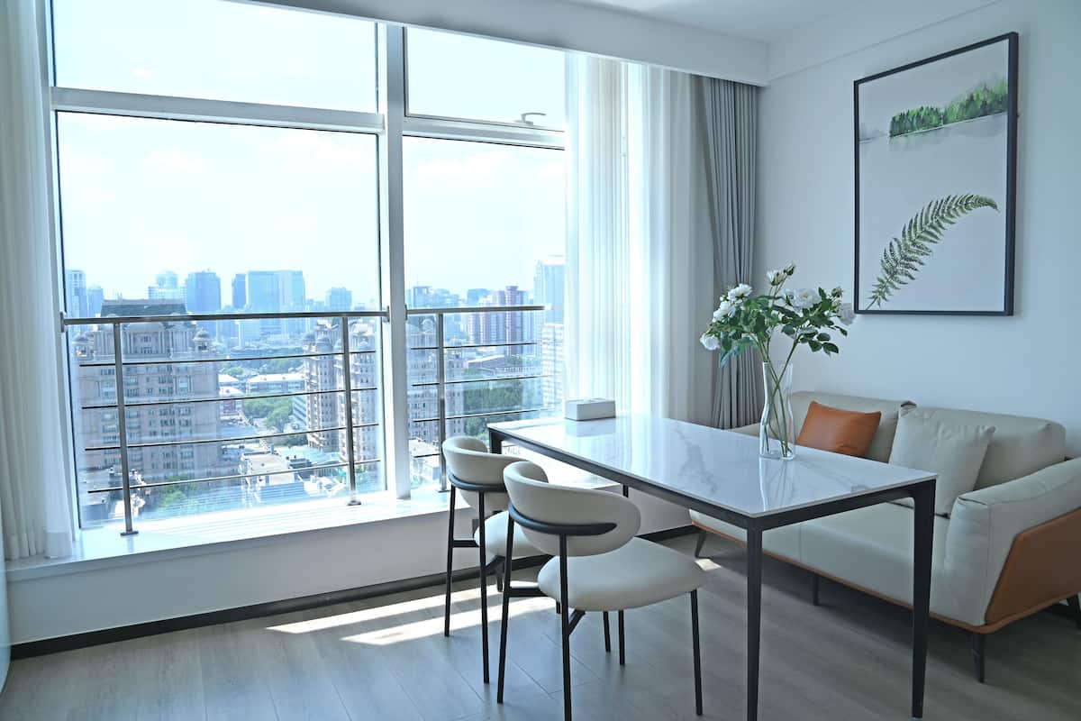 Una sala de estar moderna con un ventanal grande, una mesa de comedor, dos sillas, un sofá y una planta enmarcada en la pared.