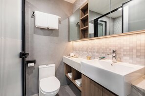 Une salle de bain moderne équipée de toilettes, d’un grand miroir, d’un lavabo et d’un porte-serviettes.