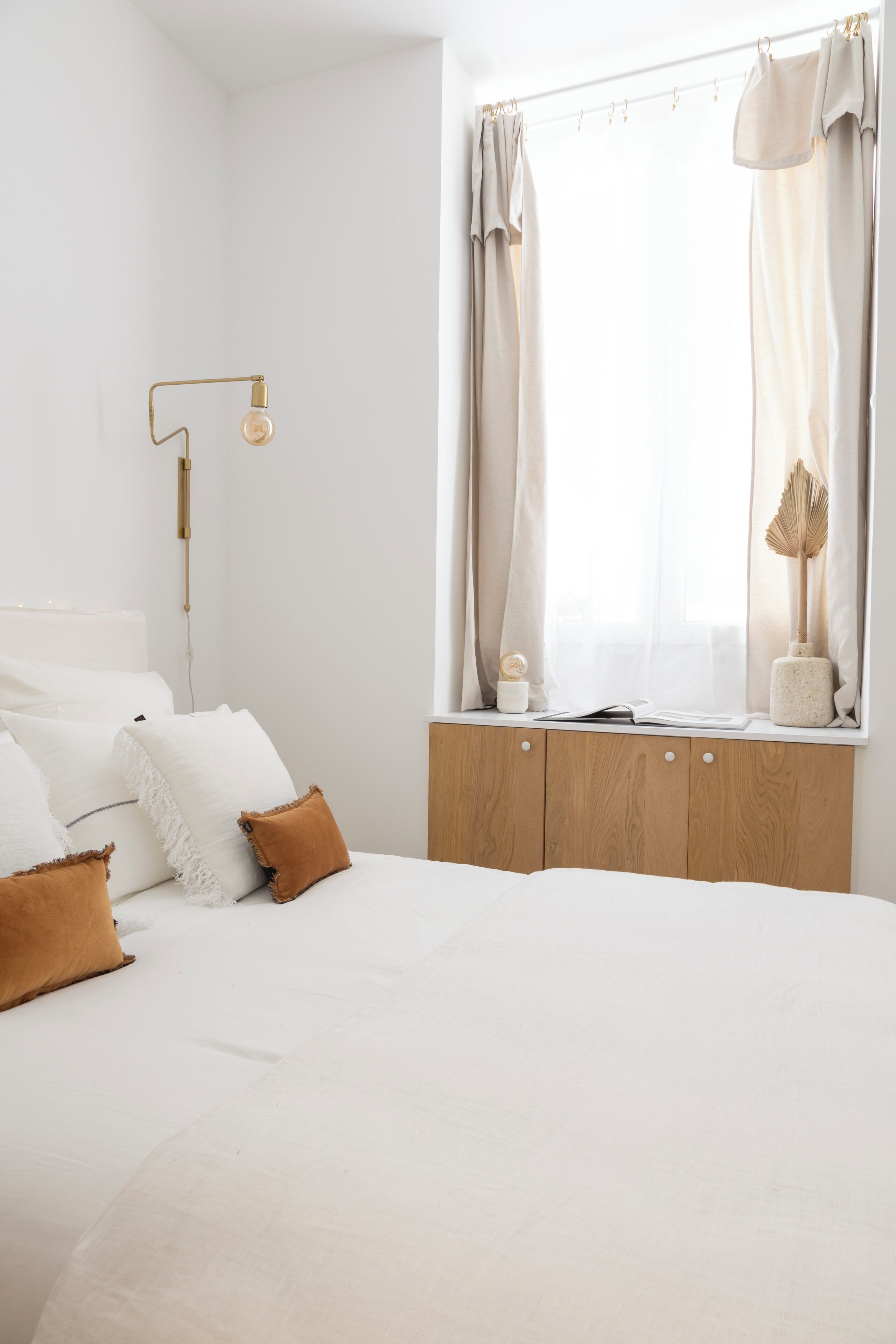 A bedroom with a bed, wooden bedside table, and a window with curtains.