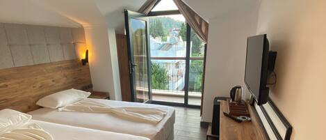 Quarto com duas camas, uma escrivaninha de madeira, televisão e varanda com vista para edifícios e vegetação.