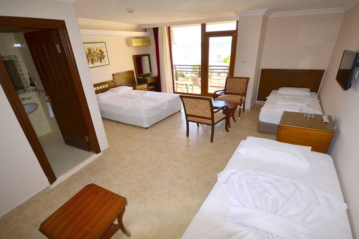 A hotel room with two beds, a wooden bench, a chair, a desk, and a balcony with a view.