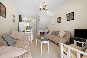 A living room with a sofa, a coffee table, a TV, and a dining area with a chair and table.