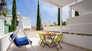 En balkon med gyngestol, et bord med stole og udsigt til omkringliggende bygninger.