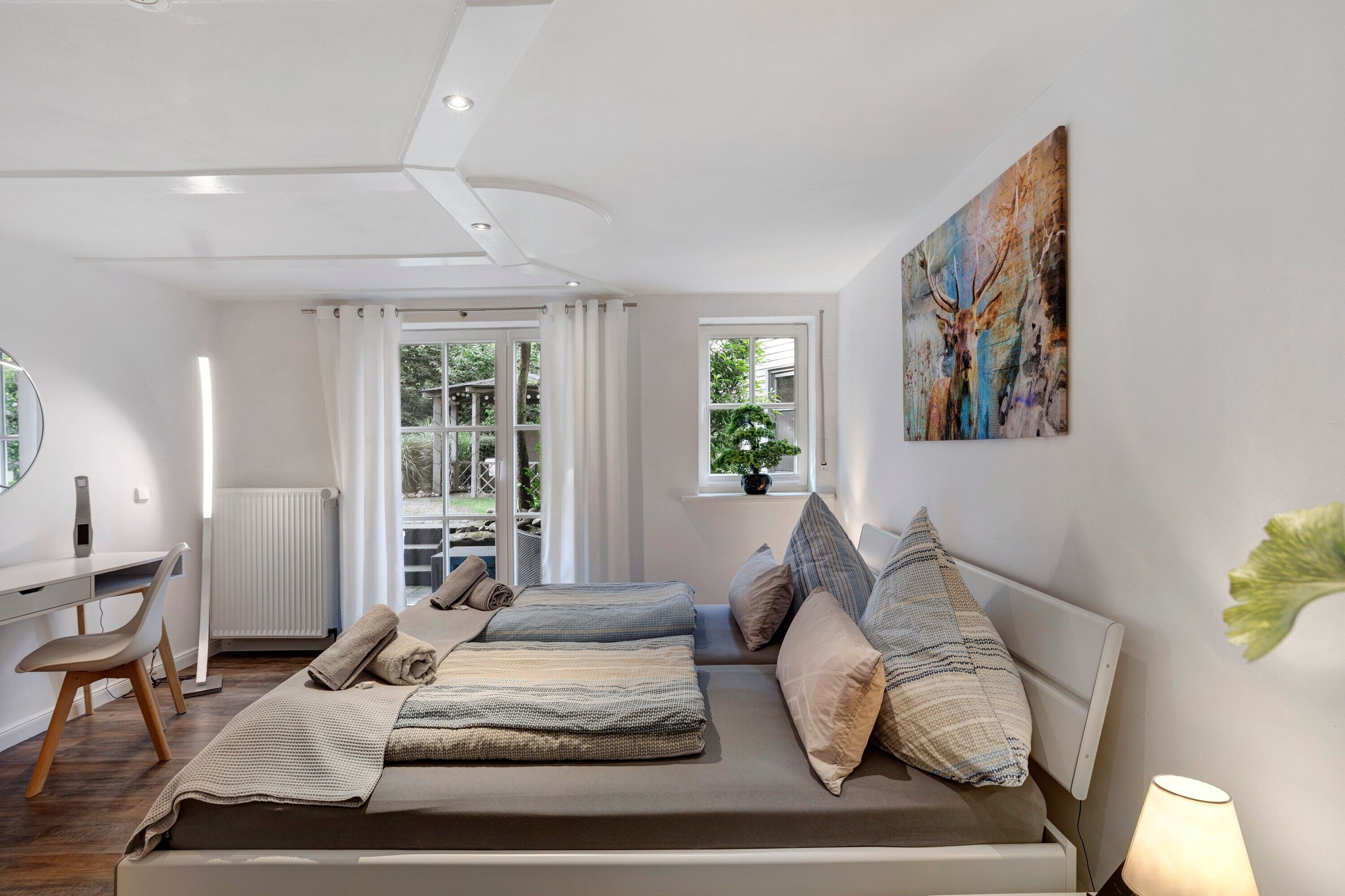 Een slaapkamer met een bed, bureau, stoel, radiator, raam met gordijnen en een schilderij aan de muur.