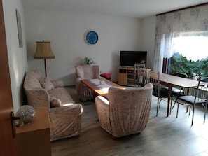 Un salon comprenant un canapé, un fauteuil, une table basse, un téléviseur et un coin repas avec des chaises et une table.
