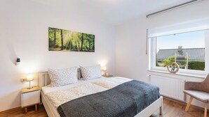 A bedroom with a bed, bedside lamps, a window with a view, and a wall-mounted picture.