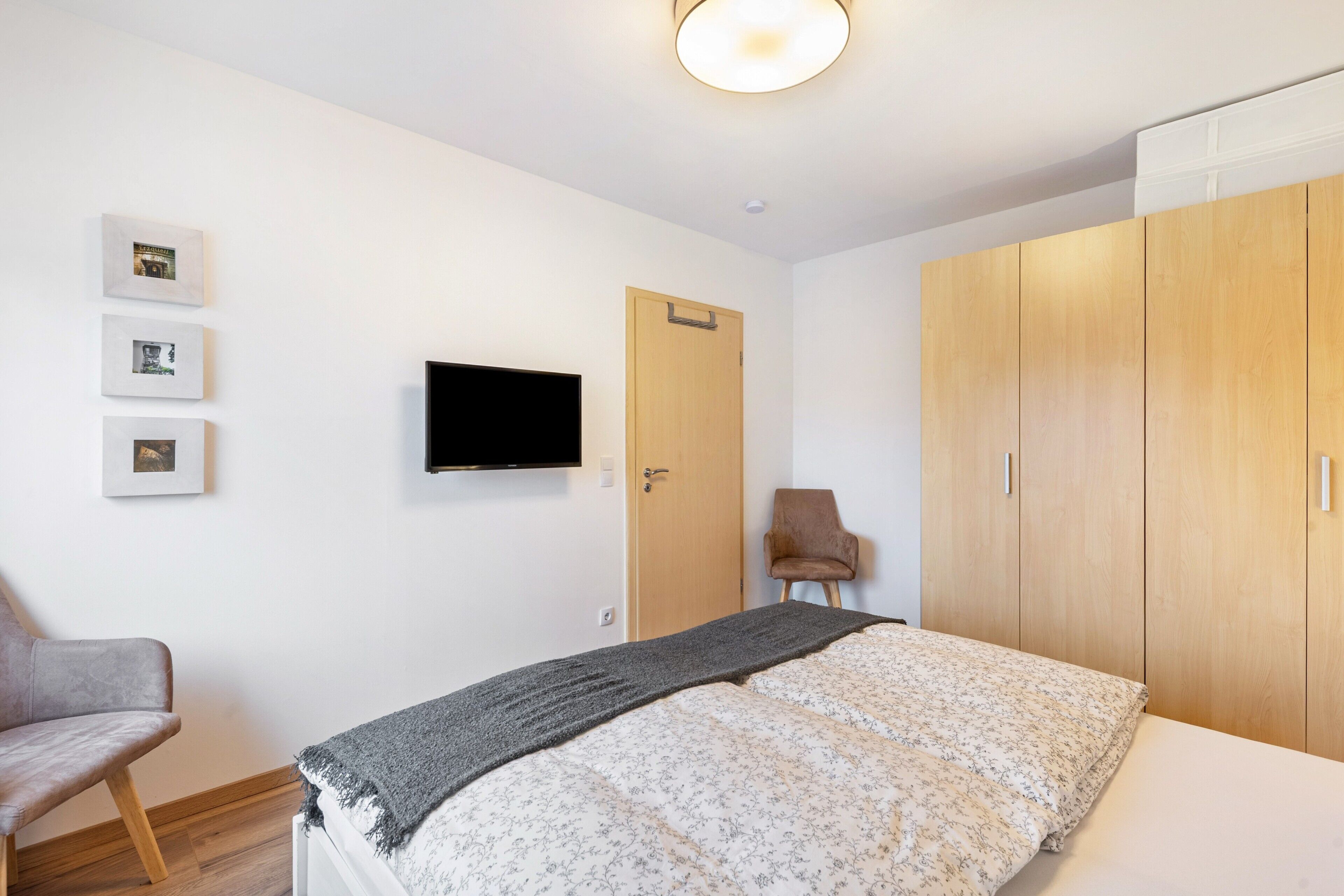 A bedroom with a bed, a TV mounted on the wall, a wardrobe, and a chair.