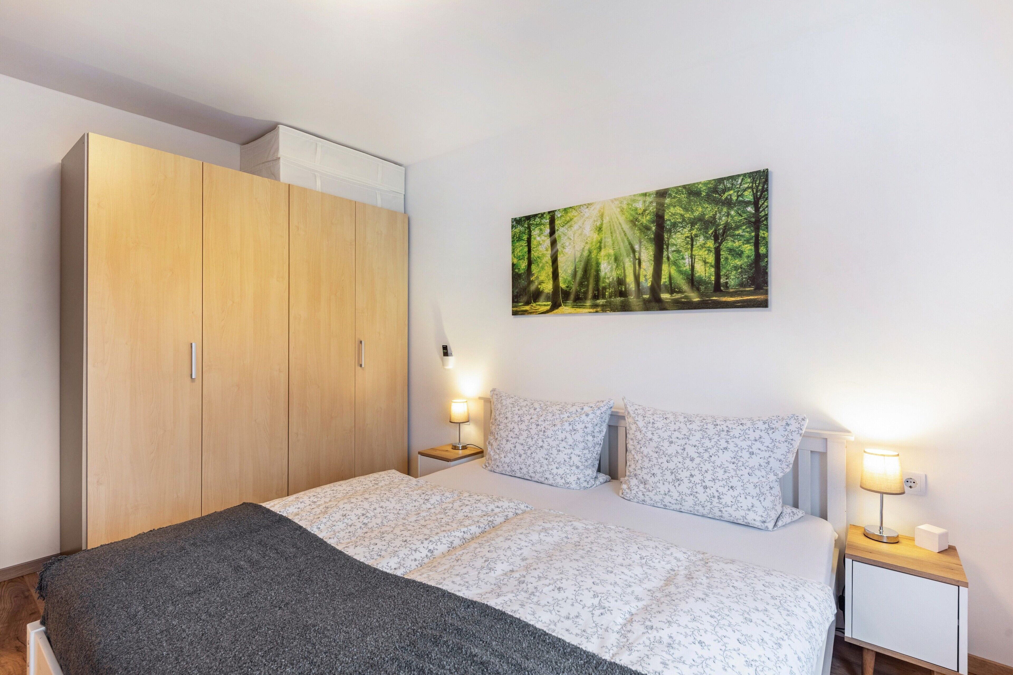 Ein Schlafzimmer mit einem Bett, zwei Nachttischen, einem Kleiderschrank und Wandbildern mit Waldmotiven.