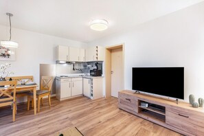 Eine moderne Küche mit weißen Schränken, ein Essbereich mit einem Holztisch und Stühlen sowie ein Fernseher auf einem Holzschrank.