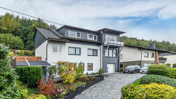 A modern two-story house with a paved driveway, a balcony, and a garage.
