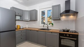 Une cuisine moderne avec des meubles gris, une cuisinière noire et une fenêtre donnant sur des immeubles.
