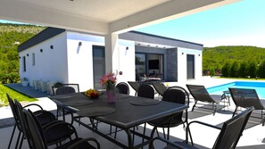 A modern outdoor dining area with a pool, surrounded by a white building with large windows.