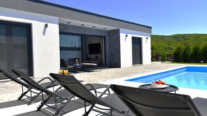 Ein modernes Haus mit Pool, Sitzgelegenheiten im Freien und Blick auf den Wald.