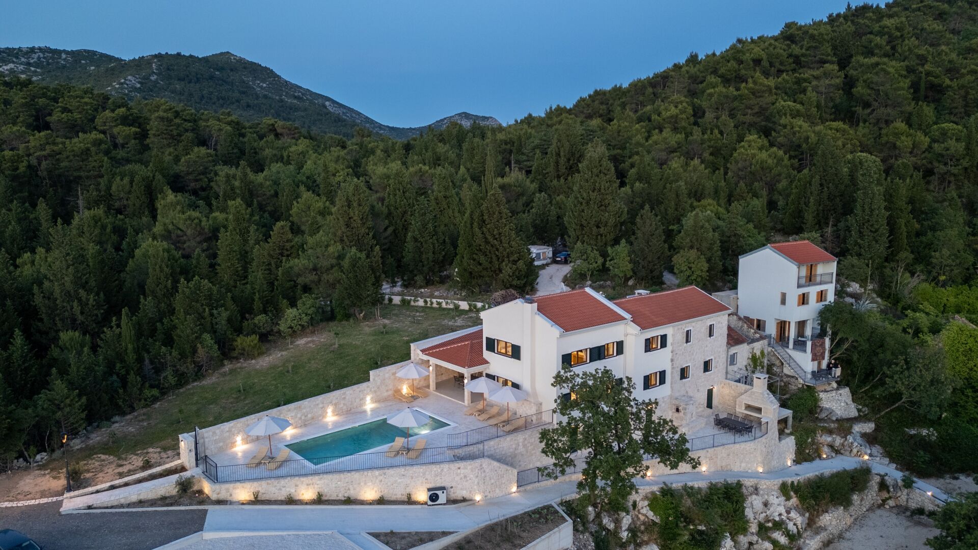 A modern villa with a swimming pool, multiple balconies, and a stone retaining wall.