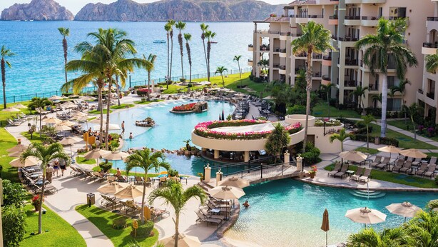 Ett semesterhotell med en stor pool, palmer och utsikt över havet.
