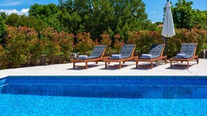 A pool with four wooden lounge chairs and a white umbrella.