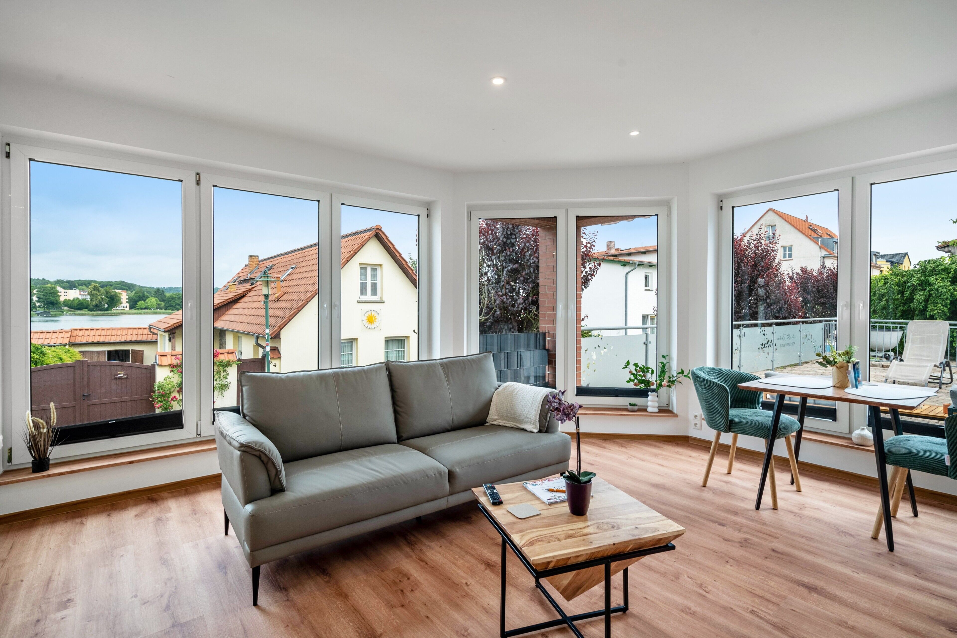 En moderne stue med sofa, sofabord og spiseplads med stole. Store vinduer giver udsigt til kvarteret.