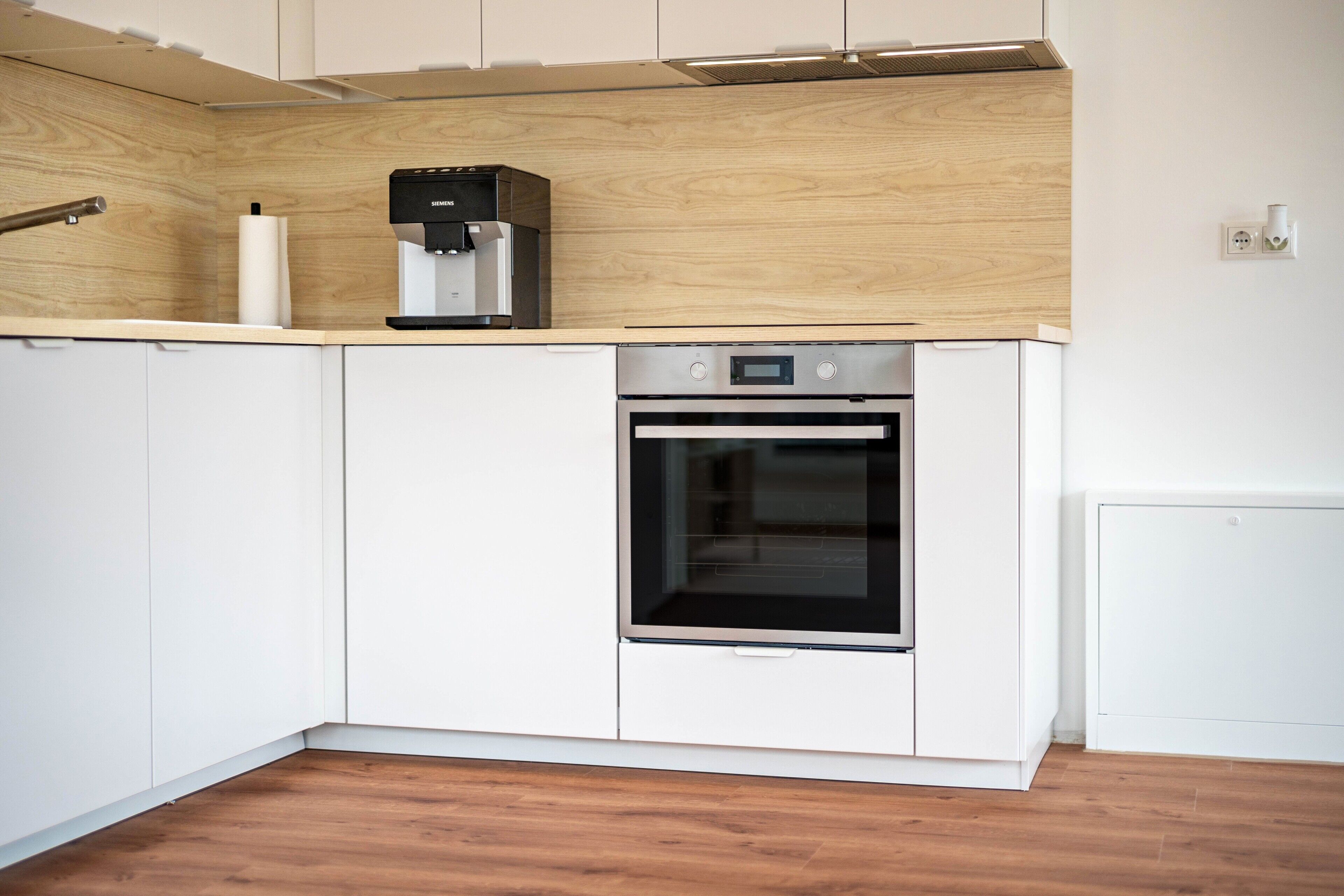 Una cocina con armarios blancos, horno de acero inoxidable y cafetera.