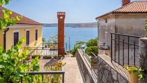 A coastal building with a brick tower, a balcony with potted plants, and a view of the sea.