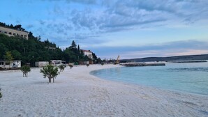 A beach with a sandy shore, a clear sky, and buildings in the background.