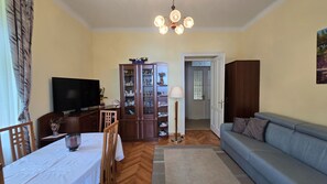 Een woonkamer met een televisie, een kast, een bank en een eettafel.