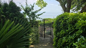 A garden pathway leading to a gated entrance with lush greenery on both sides.