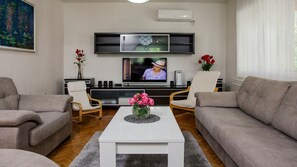Una sala de estar con una televisión de pantalla plana, dos sofás, una mesa de centro y un mueble para la televisión con altavoces.