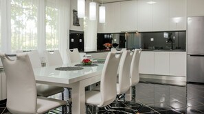 Una cocina moderna con armarios blancos, una mesa de comedor de vidrio y sillas blancas.