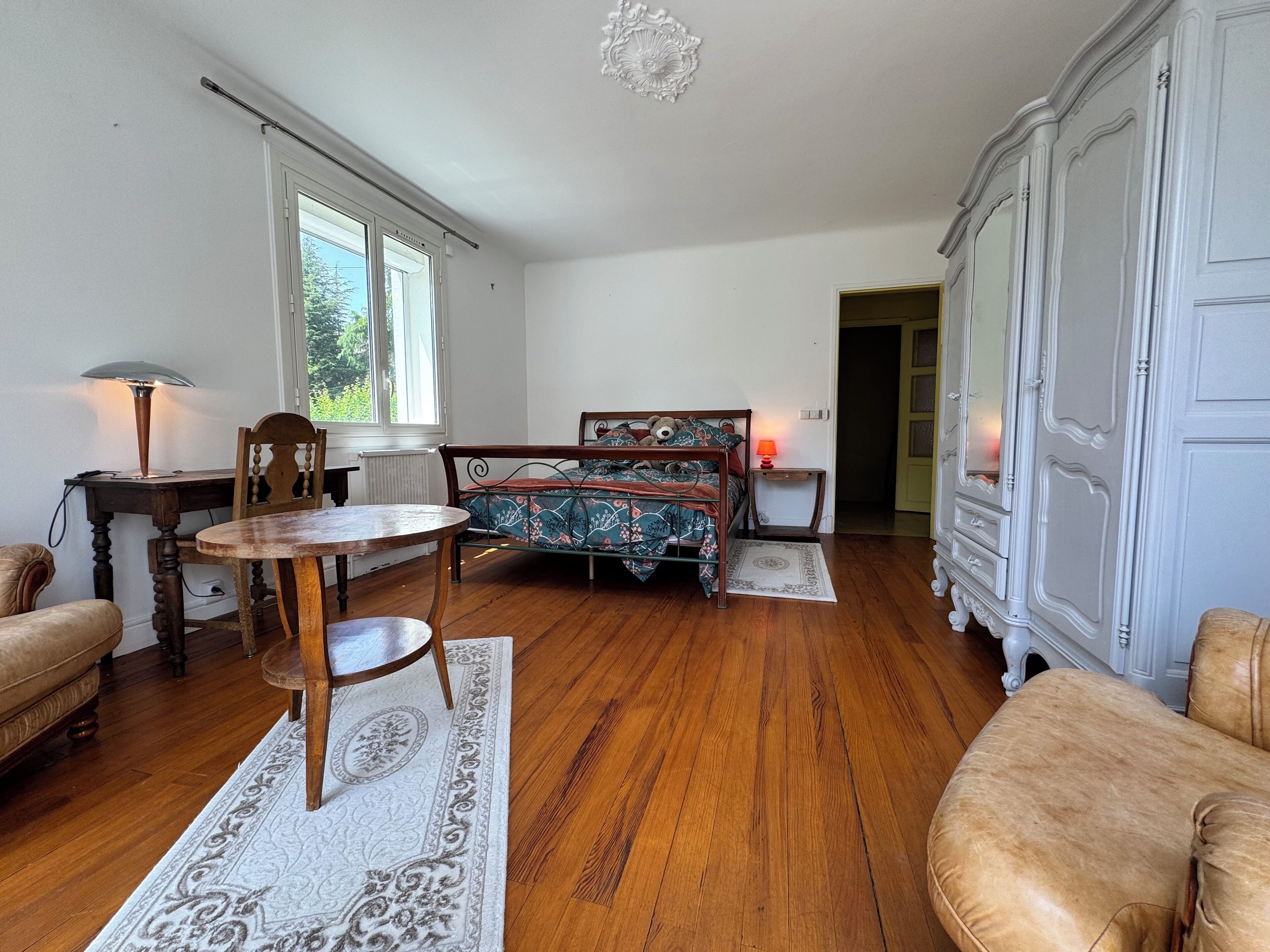 Una habitación con cama, una mesa de madera, una silla, una lámpara y un armario.