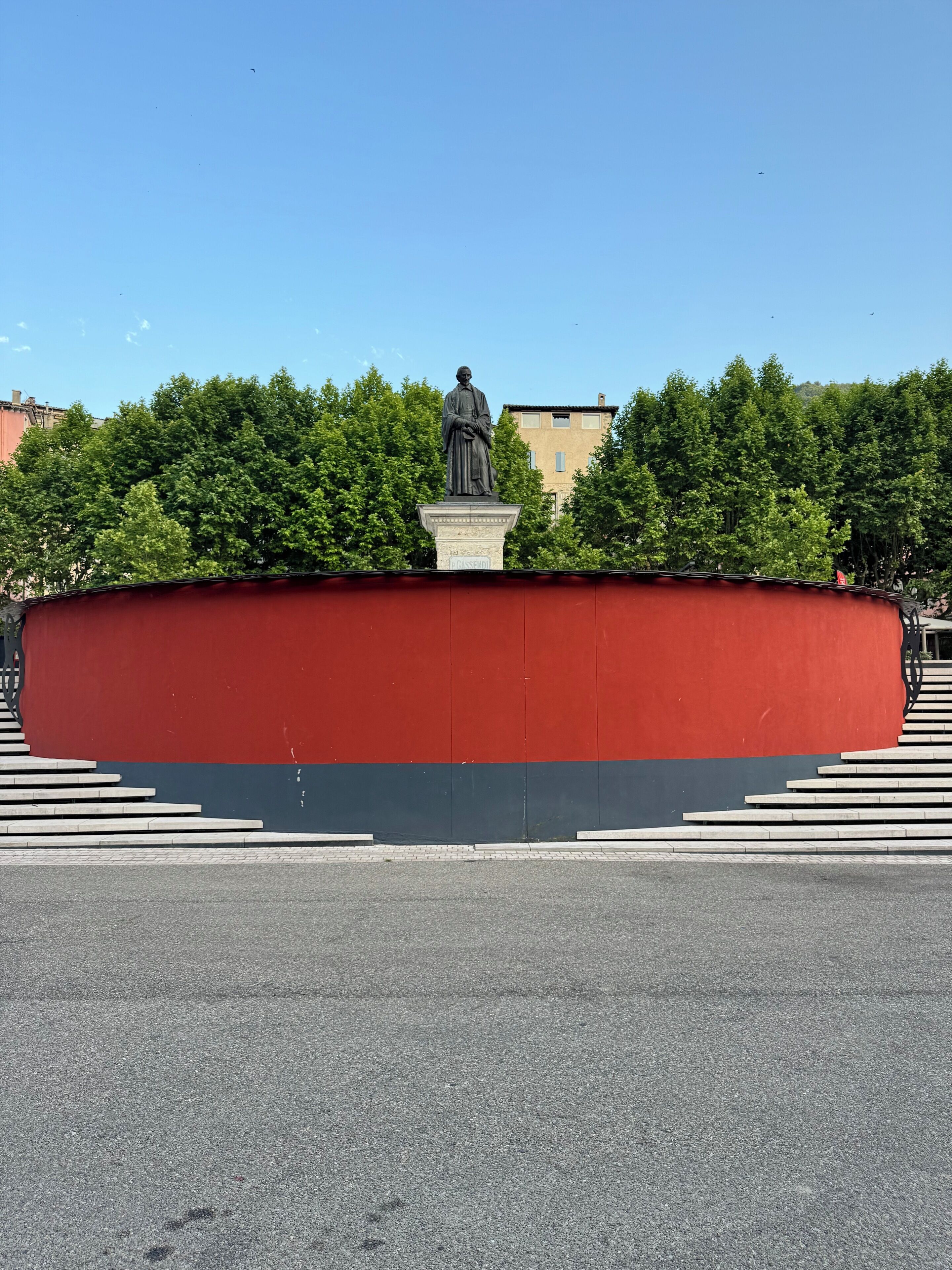 Eine Statue auf einem Sockel, mit einer roten und schwarzen Wand im Hintergrund.