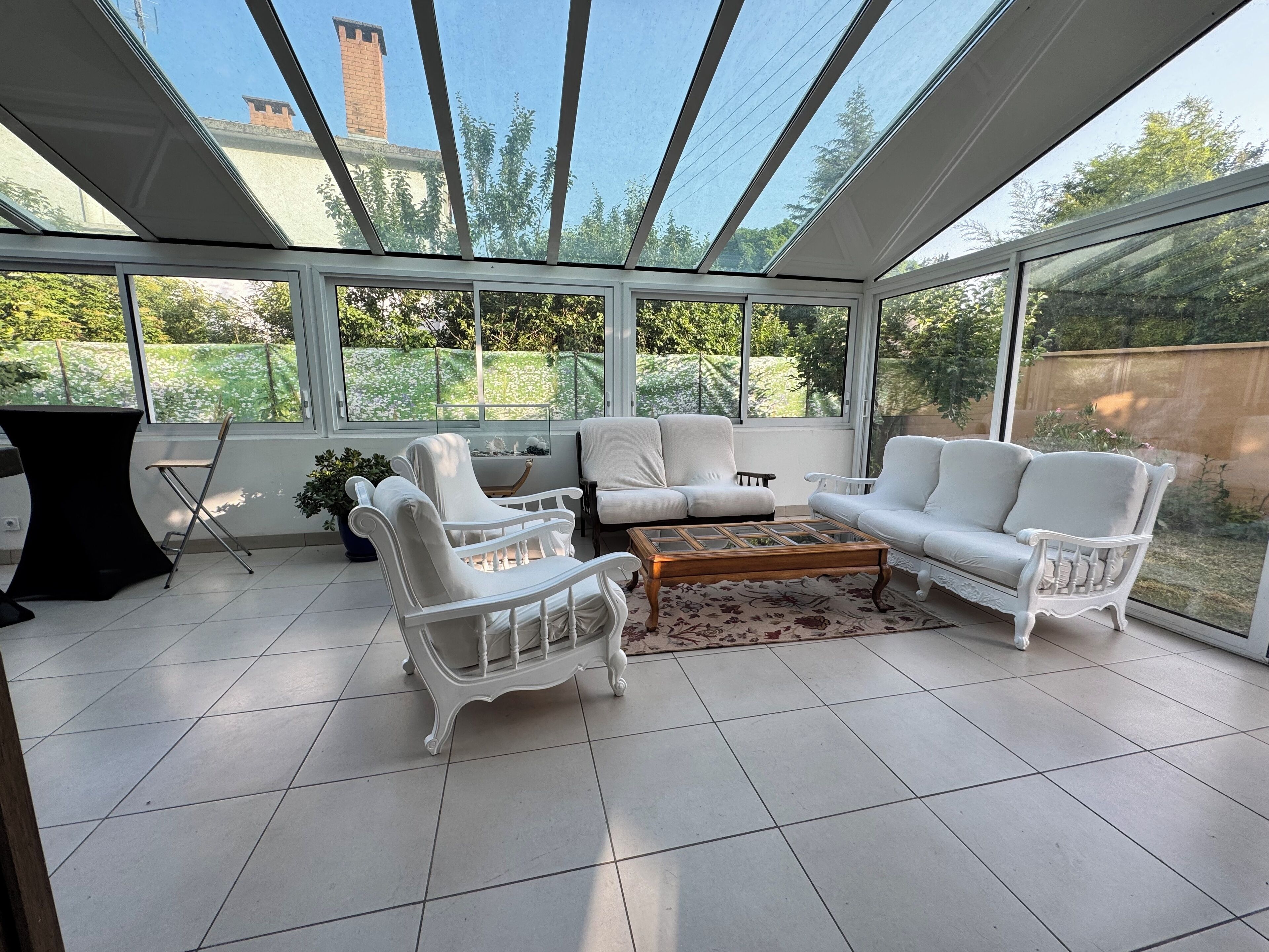 Ein Wintergarten mit weißer Möbel, darunter Sofas, Sessel, ein Couchtisch und ein kleiner Tisch mit Stühlen.