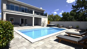 Una moderna casa a due piani con piscina, area salotto all'aperto e giardino.