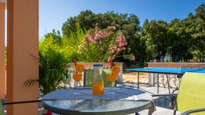 Une table ronde en verre recouverte d’une nappe bleue, deux verres contenant des boissons avec des tranches d’orange, et une bouteille de jus d’orange.