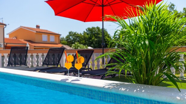 Une piscine avec des chaises longues et un parasol rouge.