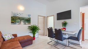 Un salon moderne comprenant un canapé, une table à manger avec des chaises, un téléviseur fixé au mur et une grande fenêtre offrant une vue panoramique.