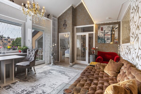 A spacious living area with a large window, a chandelier, a red sofa, and a wall-mounted artwork.