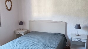 A bedroom with a wooden ceiling, a white headboard, a blue bedspread, two bedside tables with lamps, and a wall-mounted mirror. - Country house (valgorge)