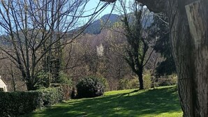 A grassy outdoor area with trees and a view of mountains in the background. - Country house (valgorge)