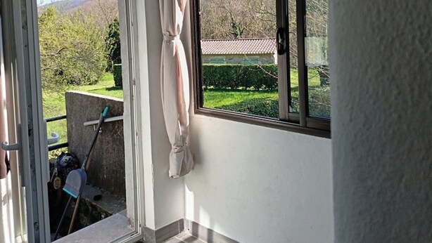 A room with a large window, a door leading outside, and a view of a green landscape with trees and hills. - Country house (valgorge)